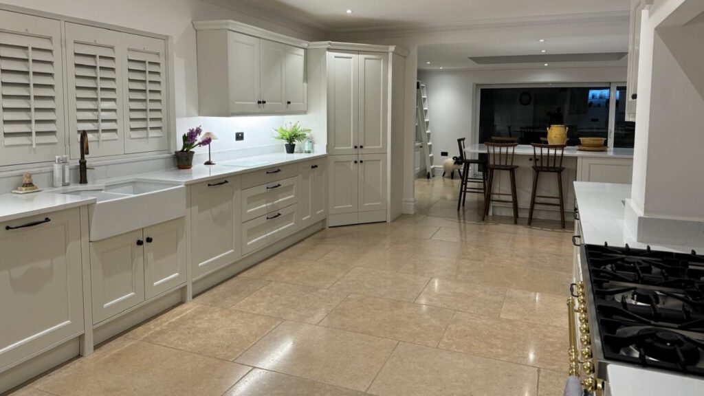 Our kitchen fitters in Swansea installed this spacious modern kitchen with cream cabinets, white countertops, tiled floor, and a breakfast bar with stools