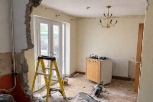Partially renovated room with exposed wall, debris on the floor, a ladder, and tools